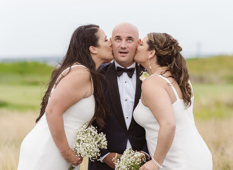 cute groom getting kisses from his sisters on wedding day