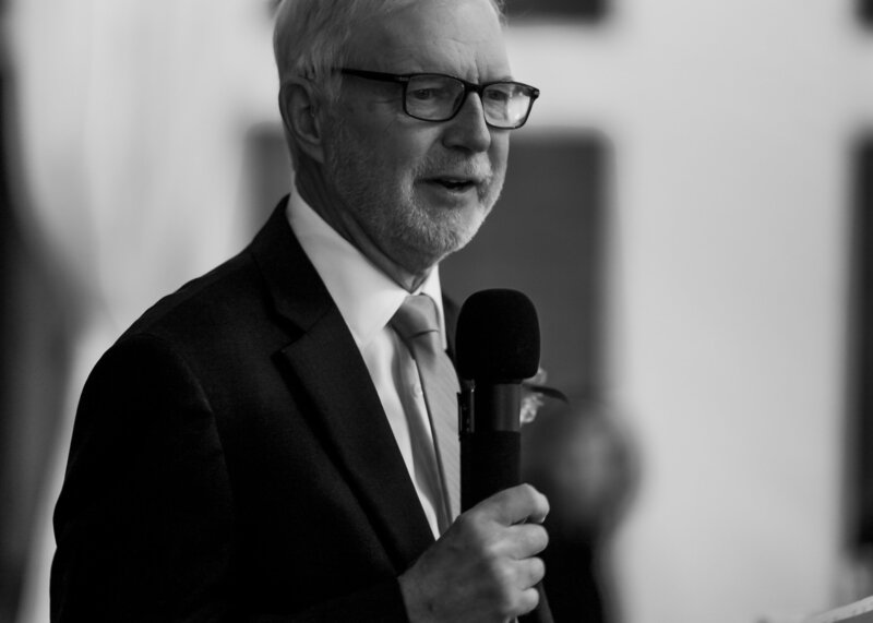 A father of a bride holding a microphone giving a speech at a reception.