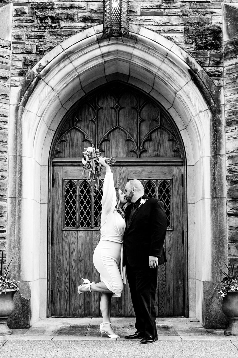 Bride kicking up her heel and holding up a bouquet after eloping at Scarritt Bennett Center in Nashville. Photo is in black and white.