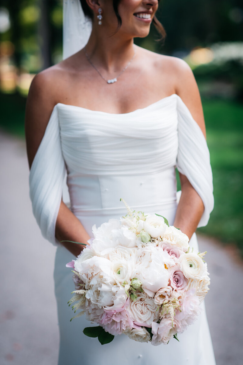 A bride in an elegant white gown holds a bouquet of white and blush flowers, showcasing the detailed planning by Savoir Fête at her Four Seasons Chicago wedding.