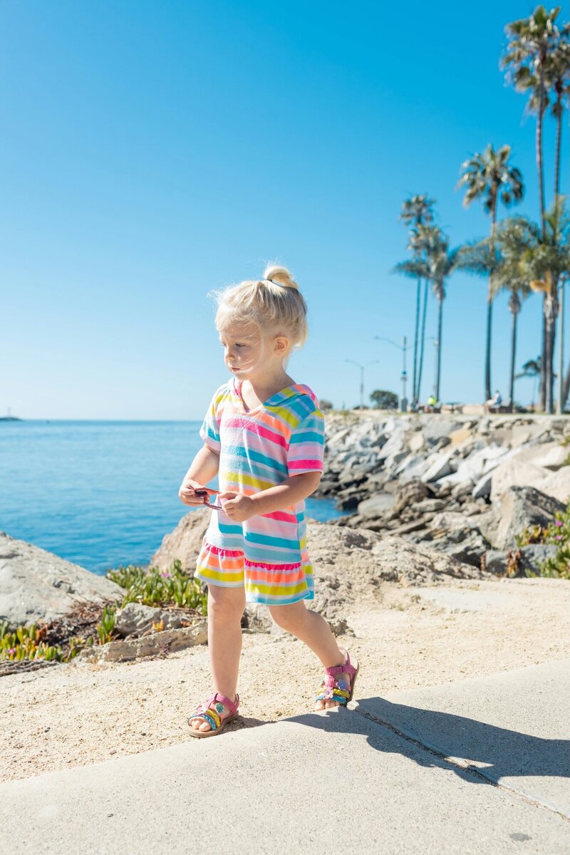 Little girl holding a pair of sunglasses as she walks along the ocean shore
