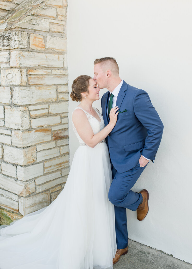 groom leaning against wall at monterey beach station wedding with his bride