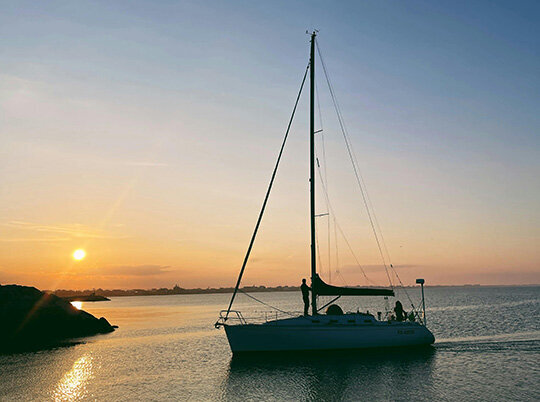 Segelyacht von oben auf dem Meer in tükisblauen Wasser und vier Menschen auf Luftmatratzen im Wasser