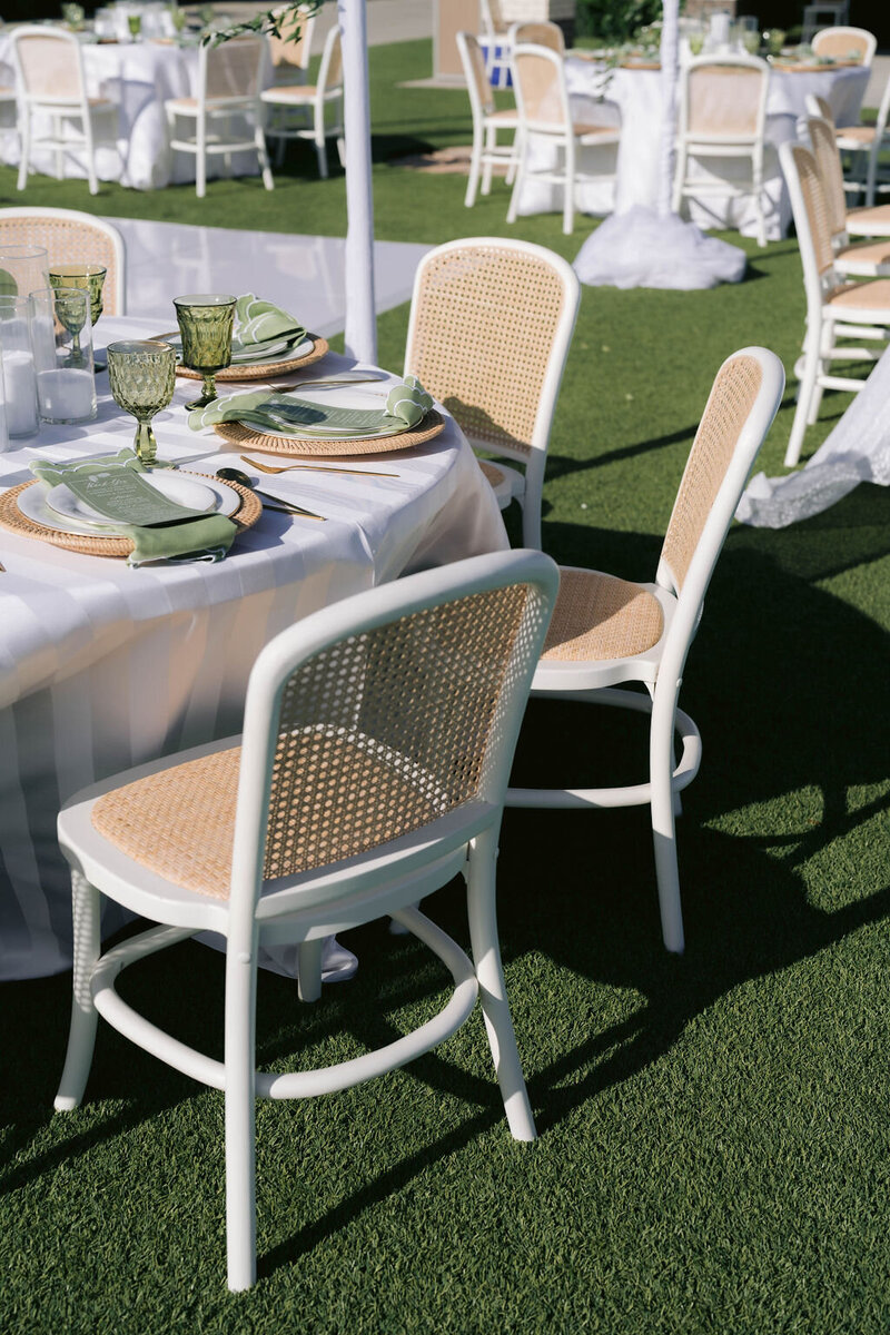 White chairs and a round table with green napkins arranged for an outdoor wedding ceremony using a standard folding round table.
