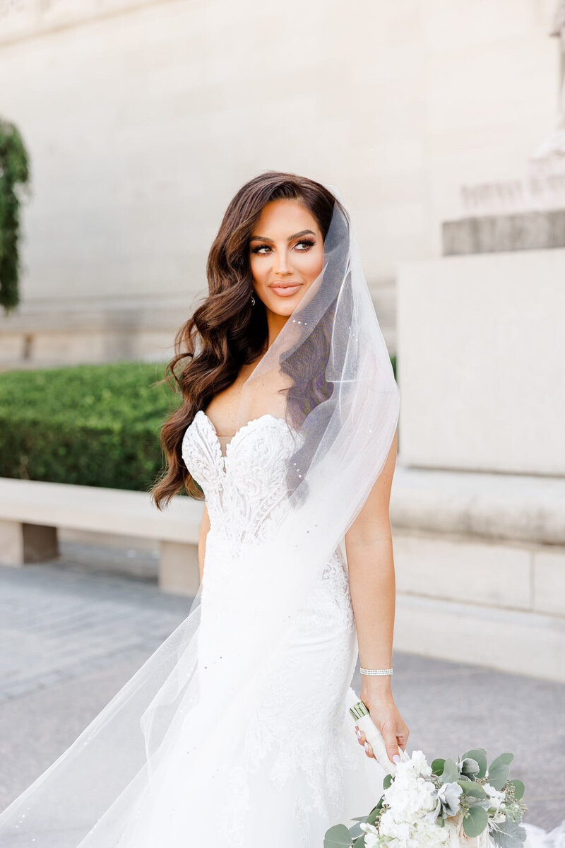 A bride in a white dress holding a bouquet of flowers down to her side.