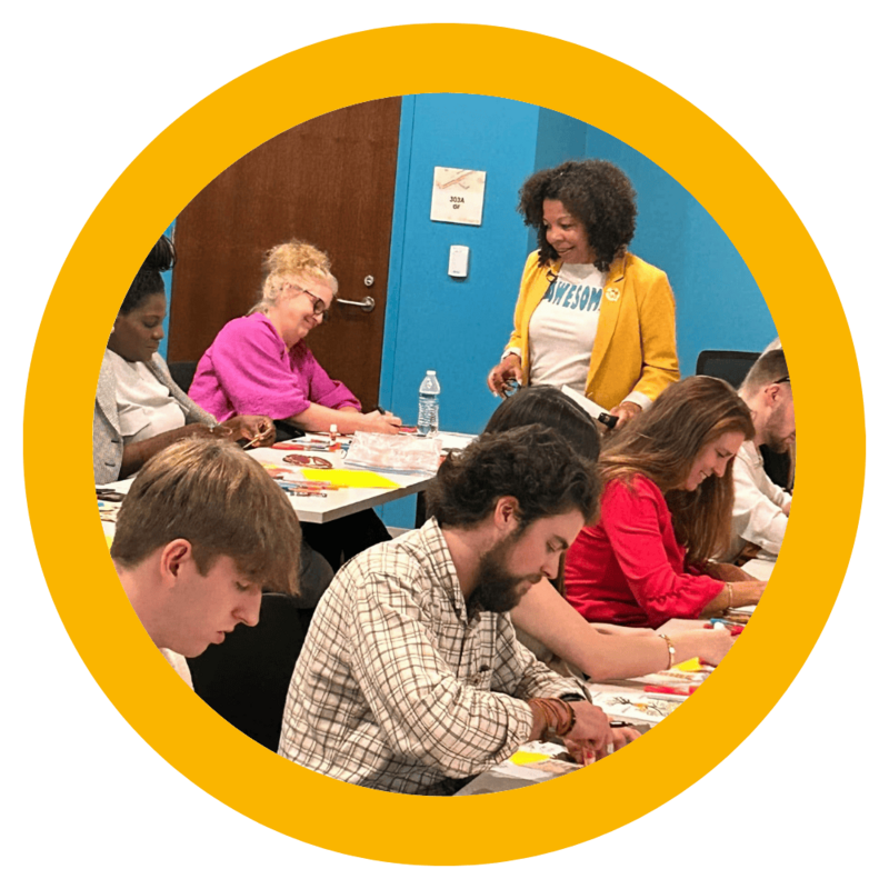 Photo of Michelle McKown-Campbell smiling while workshop participants are working on an interactive confidence building activity with construction paper