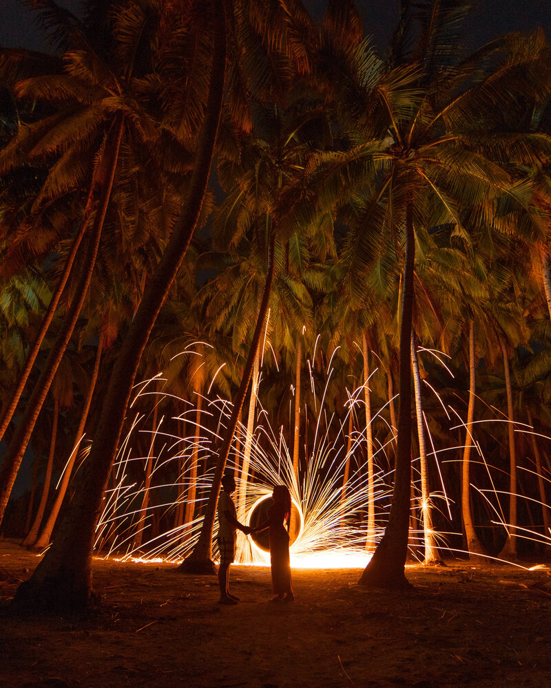 A couple are silhouetted against a catherine wheel on a beach for a wedding proposal in Barbados.