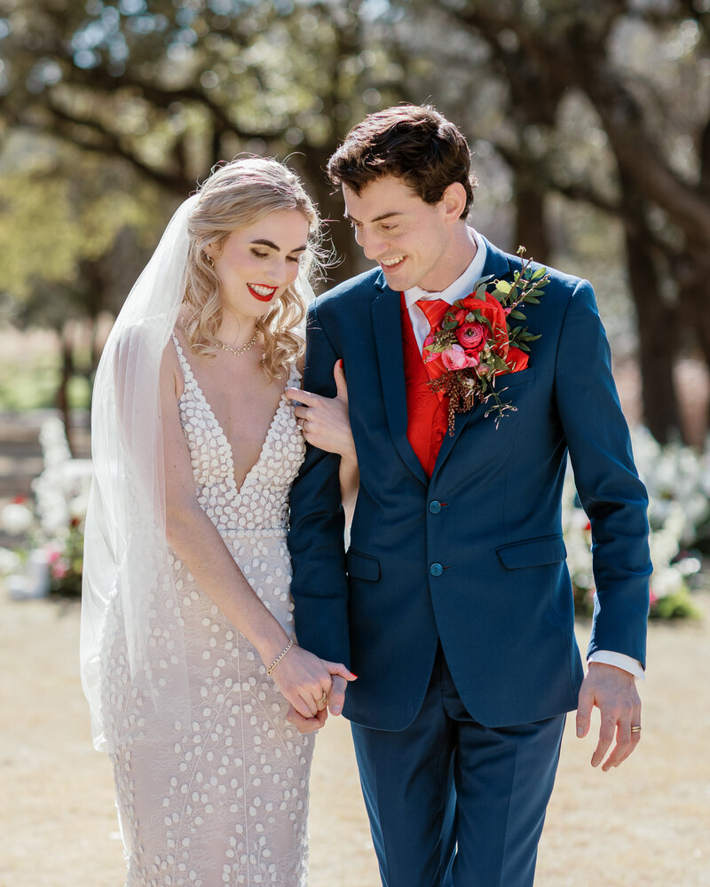 Bride and groom walk hand-in-hand in an oak-lined field during a sunny Austin wedding, planned for connection and ease.
