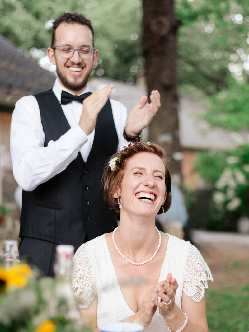 A couple laugh and clap during their wedding reception.