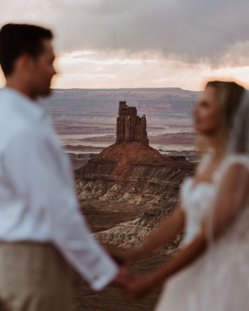 bride and groom holding hands with large rock formation and desert in the background