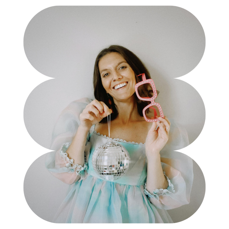 Woman holding a small disco ball on a string and holding pink glasses smiles about digitial marking for brand designers