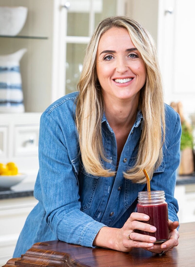 Charlotte Grand, founder of Menopause.Rescripted, smiling in the kitchen holding a smoothie