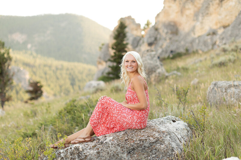 Young woman sits on a rock and smiles.