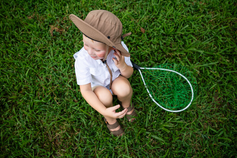 Little boy wearing a fishing hat sitting next to his fishing net birds eye view documentary portrait. 
