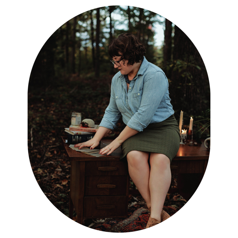 Ash sits on a table outdoors surrounded by trees and spreads out Energy Archaeology Oracle Deck cards face down 