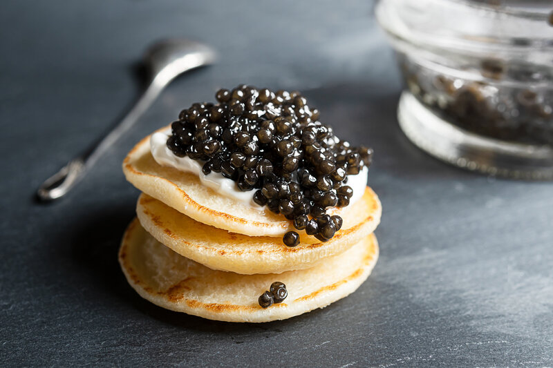 A close up photo of 3 blini pancakes stacked, with crème fraiche, and caviar on top. 