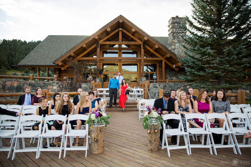 Wedding guests sit on white chairs on the back deck of the Evergreen Lake House at a fall wedding in Colorado