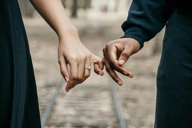 Two hands link pinkies with an engagement ring present on the woman's hand, representing an invitation to engaged couples to  the bridal show.
