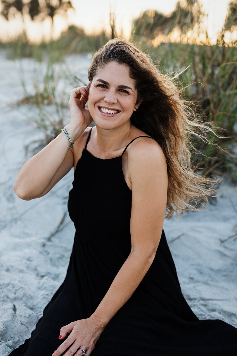 Owner of Erin Elyse Photographer in black dress sitting on beach in Atlantic Beach, FL.