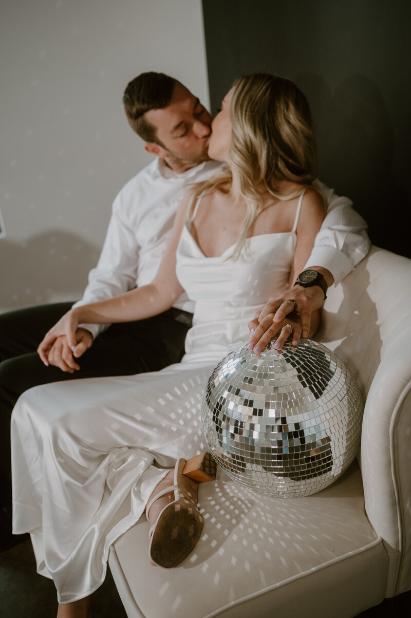 Luxury elopement Bride and groom kissing and sitting next to a disco ball