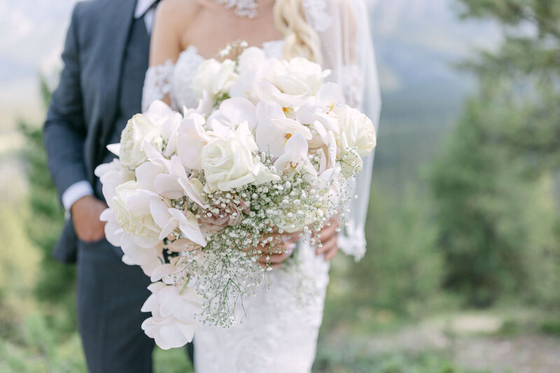 This romantic photograph captures the groom holding his bride at The Inn on Officers Garden in Calgary, with the bride elegantly holding a large bouquet of flowers, creating a timeless and beautiful moment.