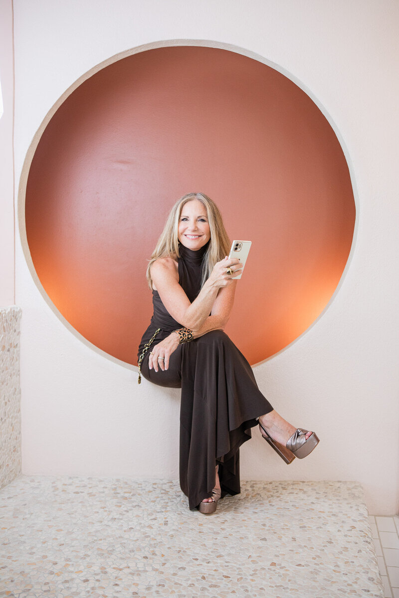Woman smiling and seated on a modern circular chair holding a phone in hand
