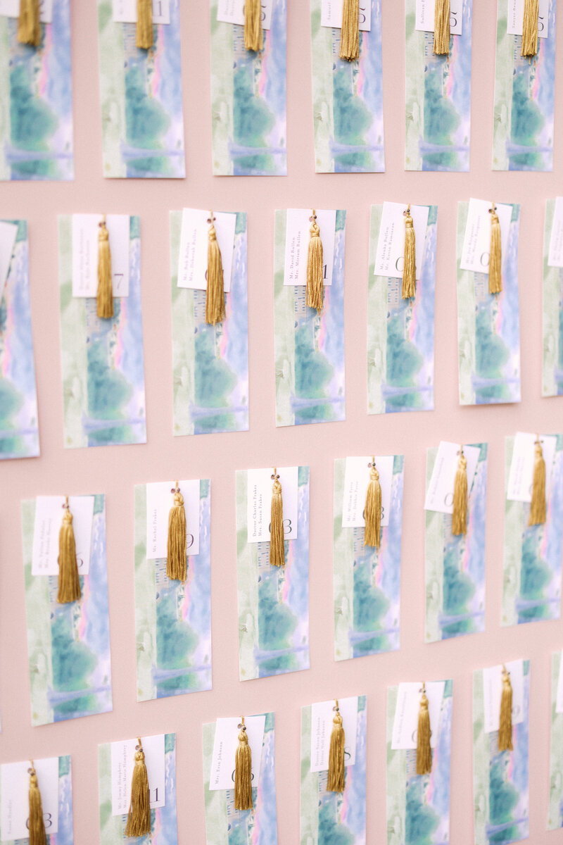 November wedding at Graylyn Estate, designed and planned by Charming Carolina — personalized bookmark escort display featuring watercolor artwork by the groom’s brother, gold tassels, table numbers, and a thank you note from the couple. Each bookmark hung on a blush board as a creative guest seating display.