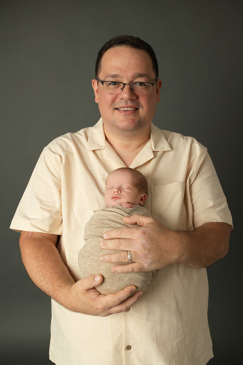 baby swaddled in a tan swaddle mom in a floral dress snuggled into her newborn baby with her eyes closed