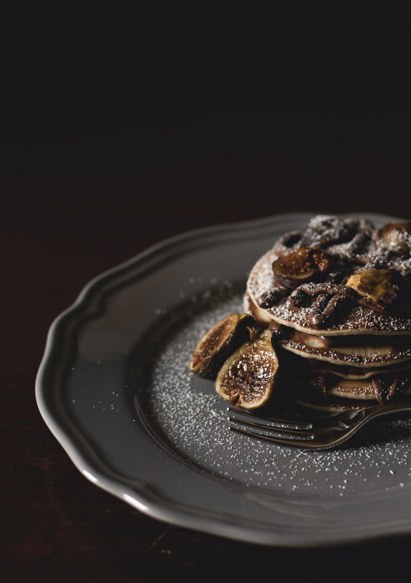 A gray plate featuring a stack of pancakes covered in figs and chocolate sauce. 