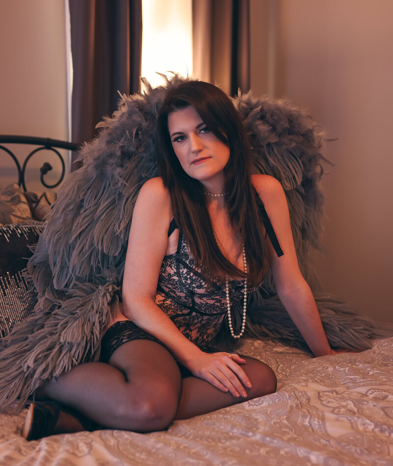 Boudoir  Portrait of brunette woman on  bed in gray angel wings