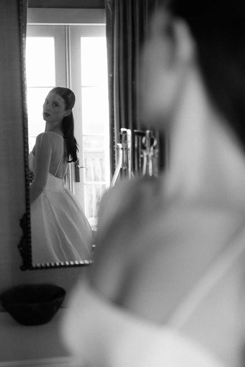 Bride glances over her shoulder in the mirror while admiring her dress. 