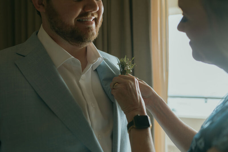 Mother of the groom pins floral on groom