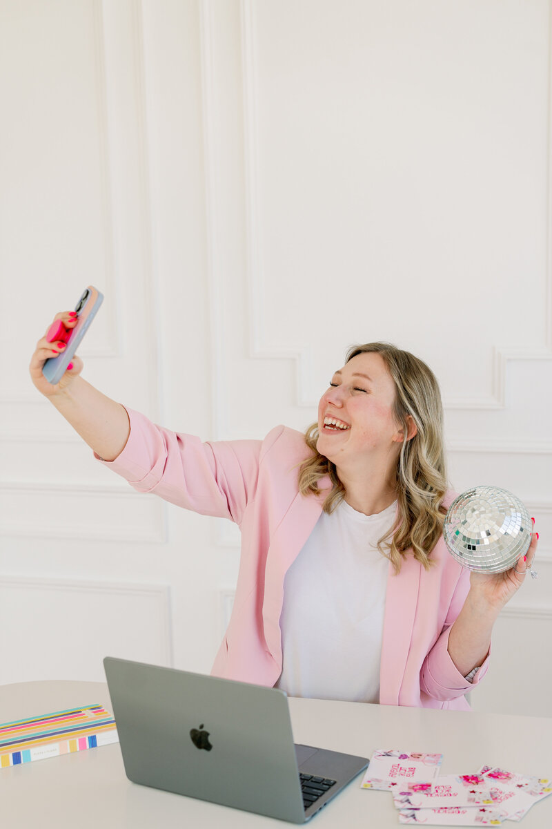 Kat Murphy in a pink jumpsuit holding an iphone