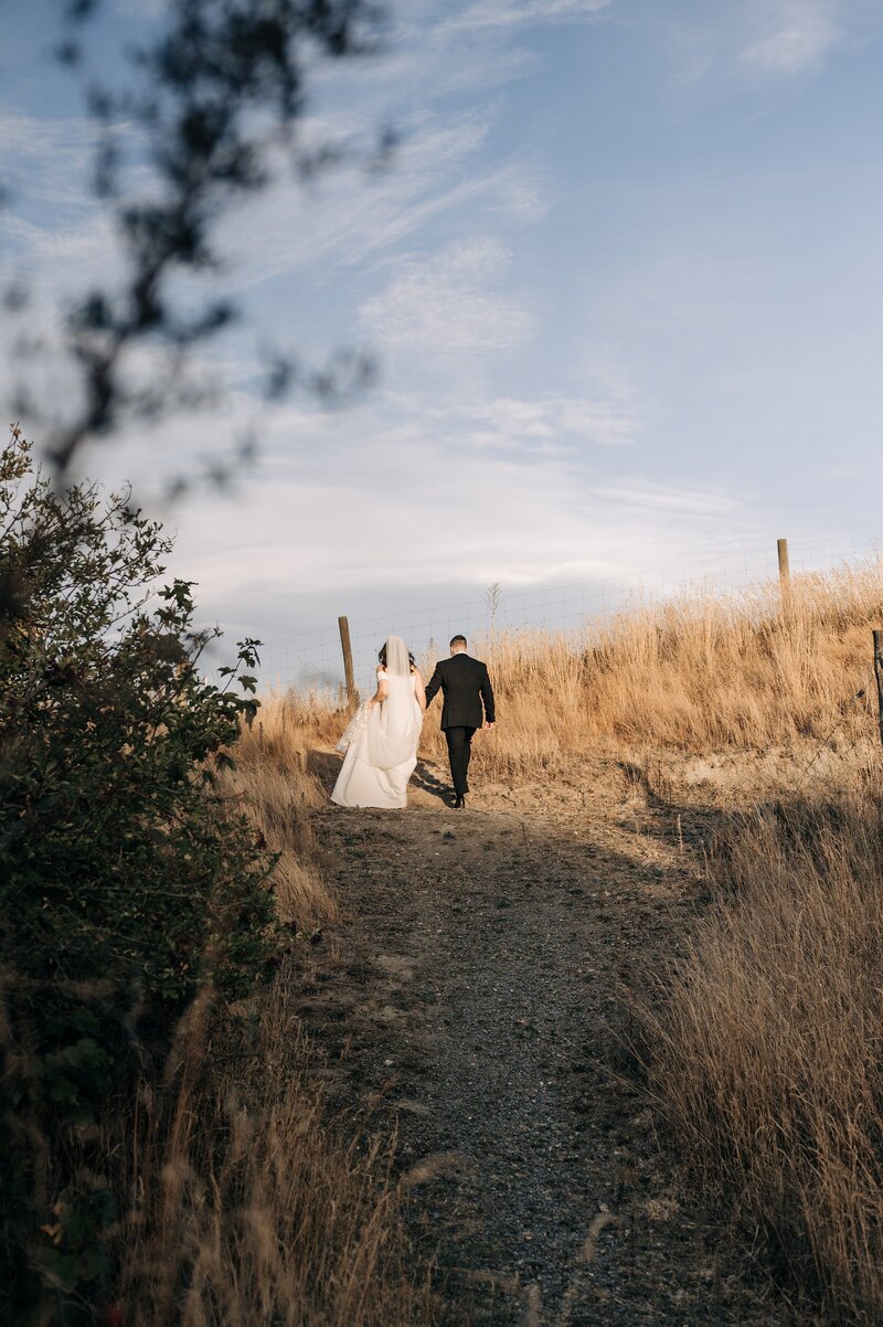 a bride and groom walk up a hill in the sunset in queenstown new zealand on their wedding day