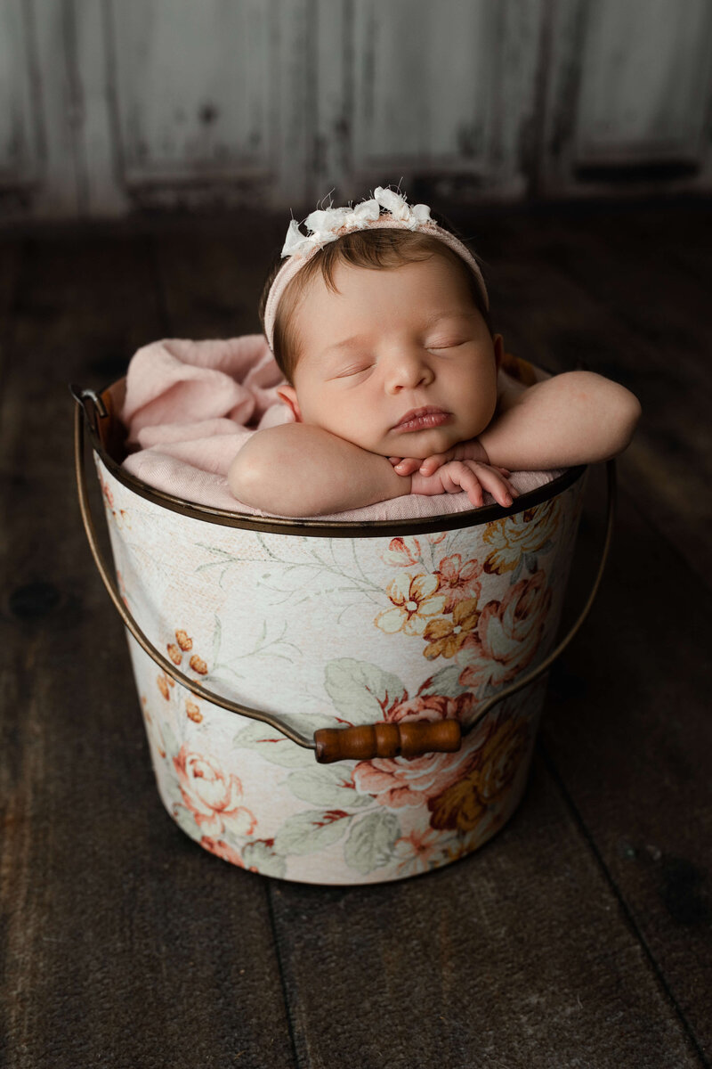 baby boy sleeping with his hands under his head in a green onesie on a green plant background newborn harrisburg photos