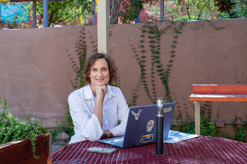 Smiling woman working outdoors at a table with her laptop, photographed by Vyrl Photo, showcasing Tucson brand photography.