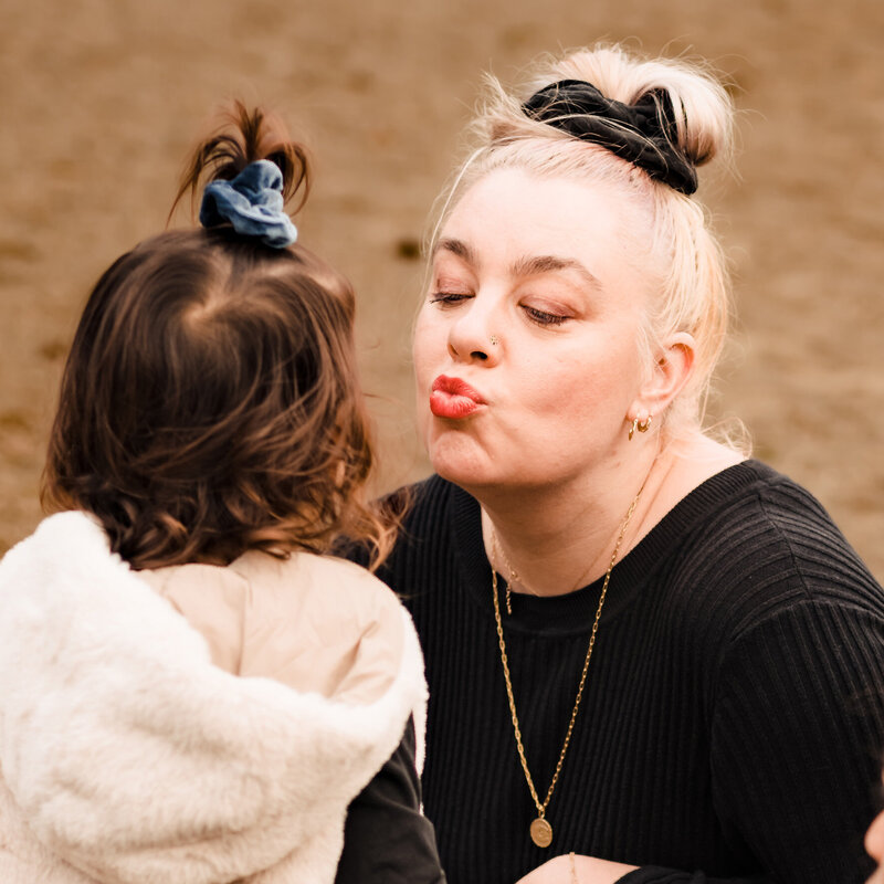 Mom kissing toddler during family photoshoot on a beach in Redmond, Washington