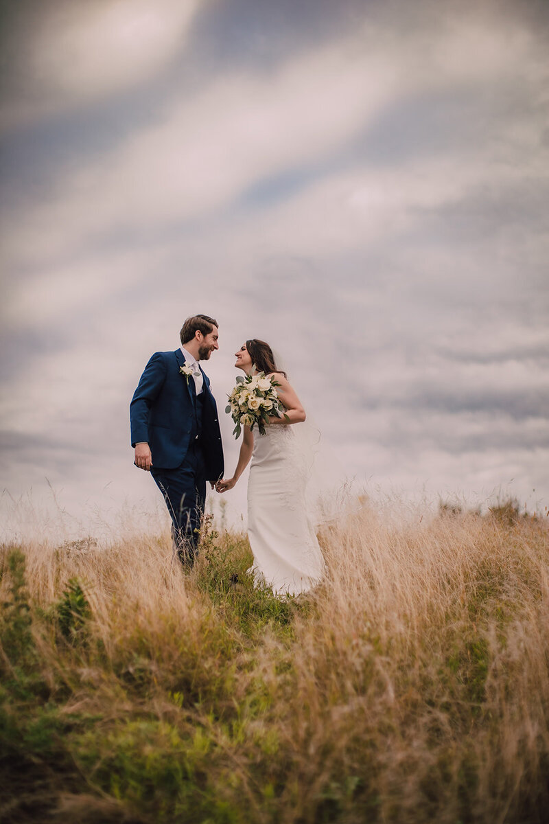 Bride and groom walk through prairie grass