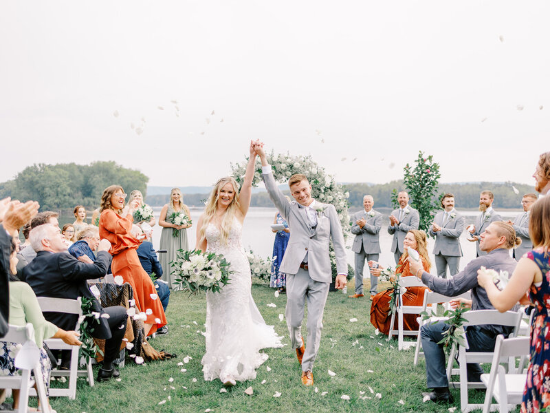 Bride and groom recess down the aisle holding hands in the air while guests clap and toss flowers into the air