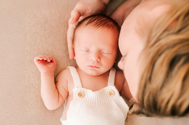 Newborn photography in Springfield MO of mom holding sleeping newborn baby in white overalls