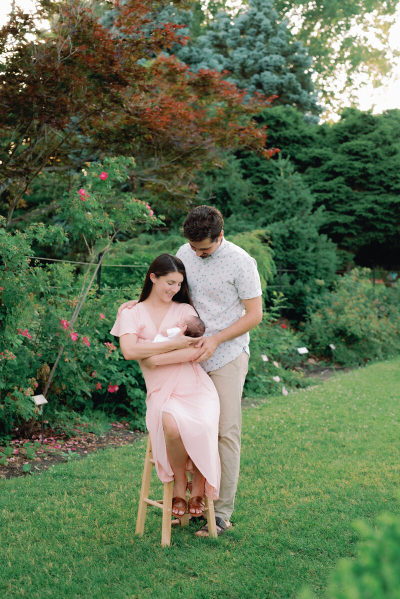 Couple sitting down and holding newborn baby in garden in Ottawa