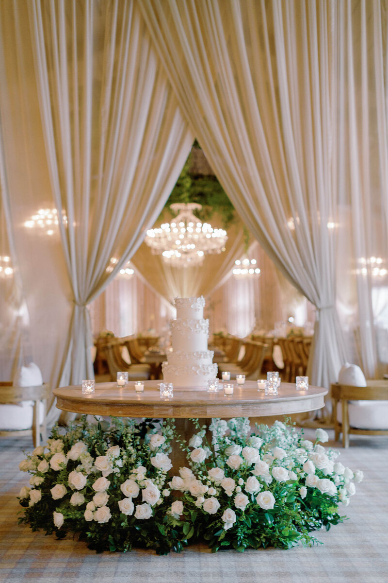 Luxury indoor wedding reception with white and green florals, custom drapery and four tiered cake
