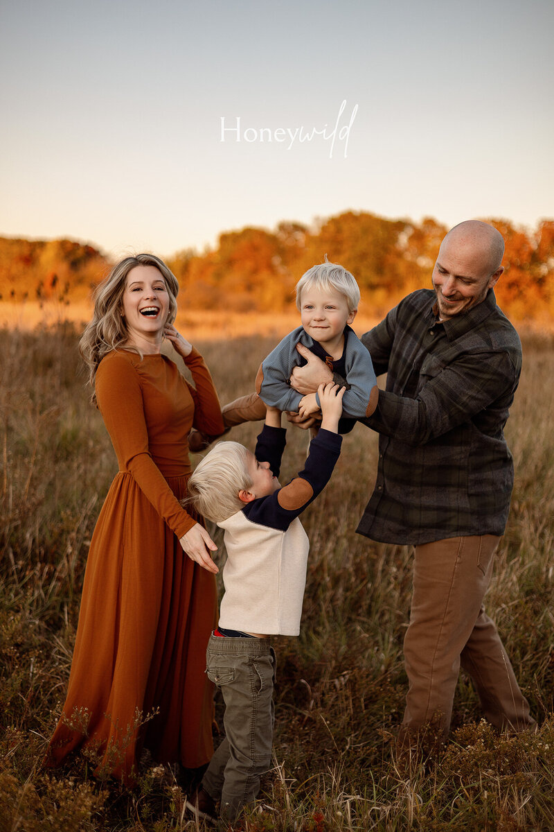  A fun and loving family of four laughing together in an outdoor setting in Grand Rapids, Michigan, during a relaxed and natural family photography session.