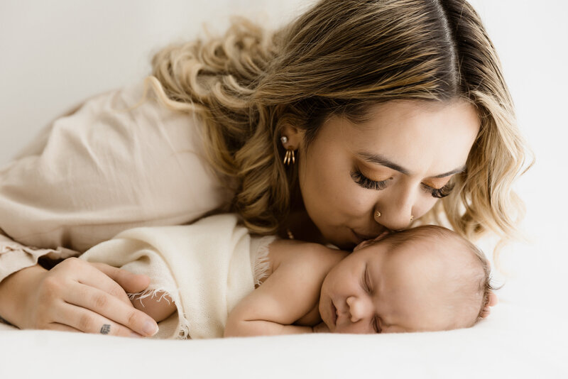 Newborn Photography Session, Mother wearing client closet outfit, and lovingly kissing her brand new baby on the ceek