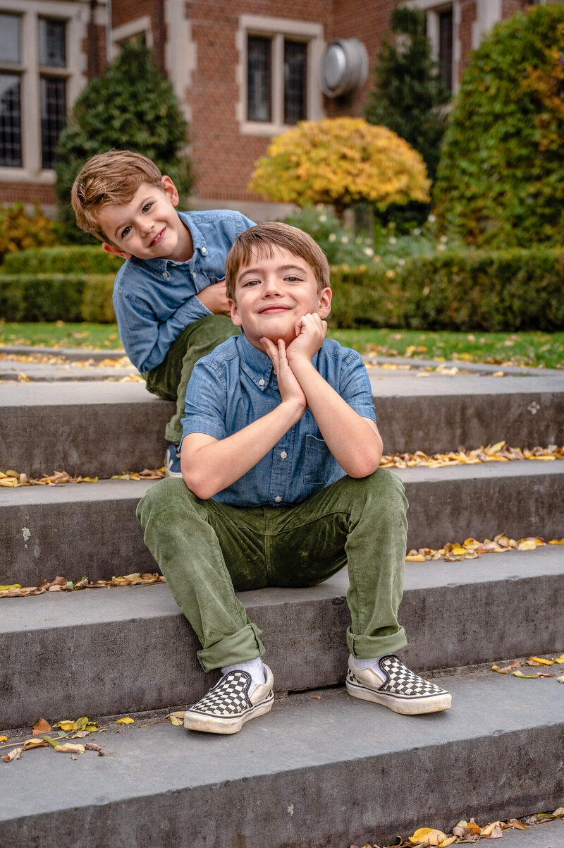 Two young brothers, sitting on a step at Waveny park in New Canaan; the younger brother a step above and being silly and peeking to one side of his brother.