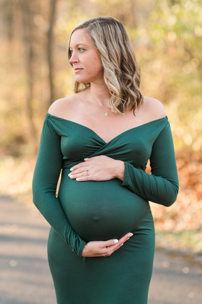Pregnant mother wearing dark green dress with hands wrapped around belly with golden light in the background in lancaster pa