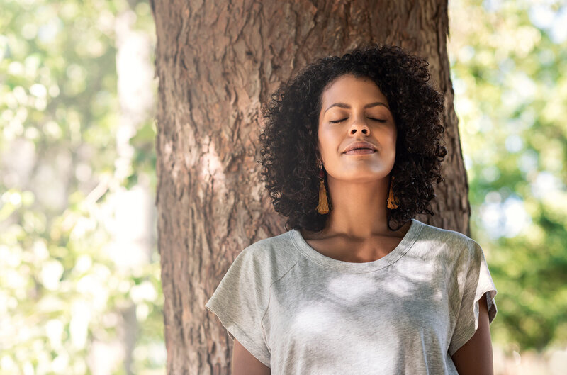 Woman with eyes closed leaning against a tree