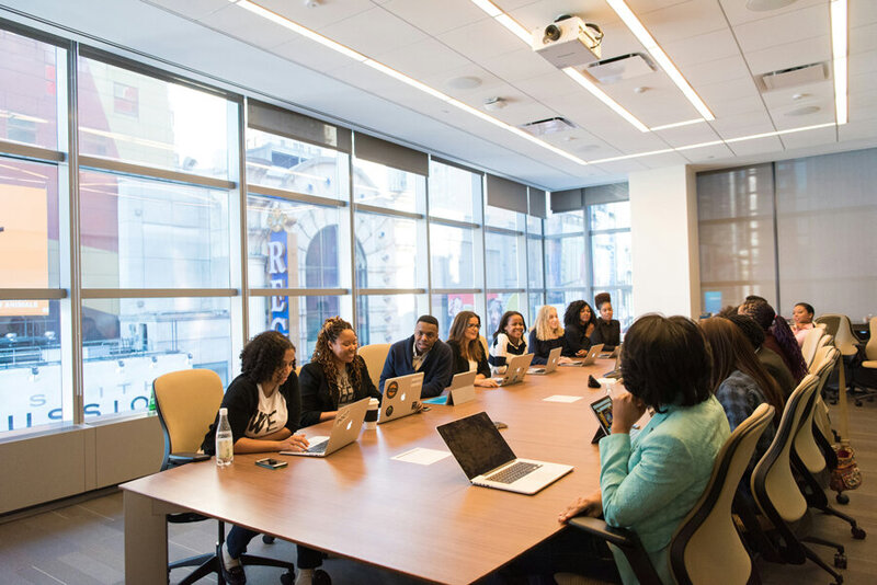 A group of Black female entrepreneurs sit around a table discussing their project.