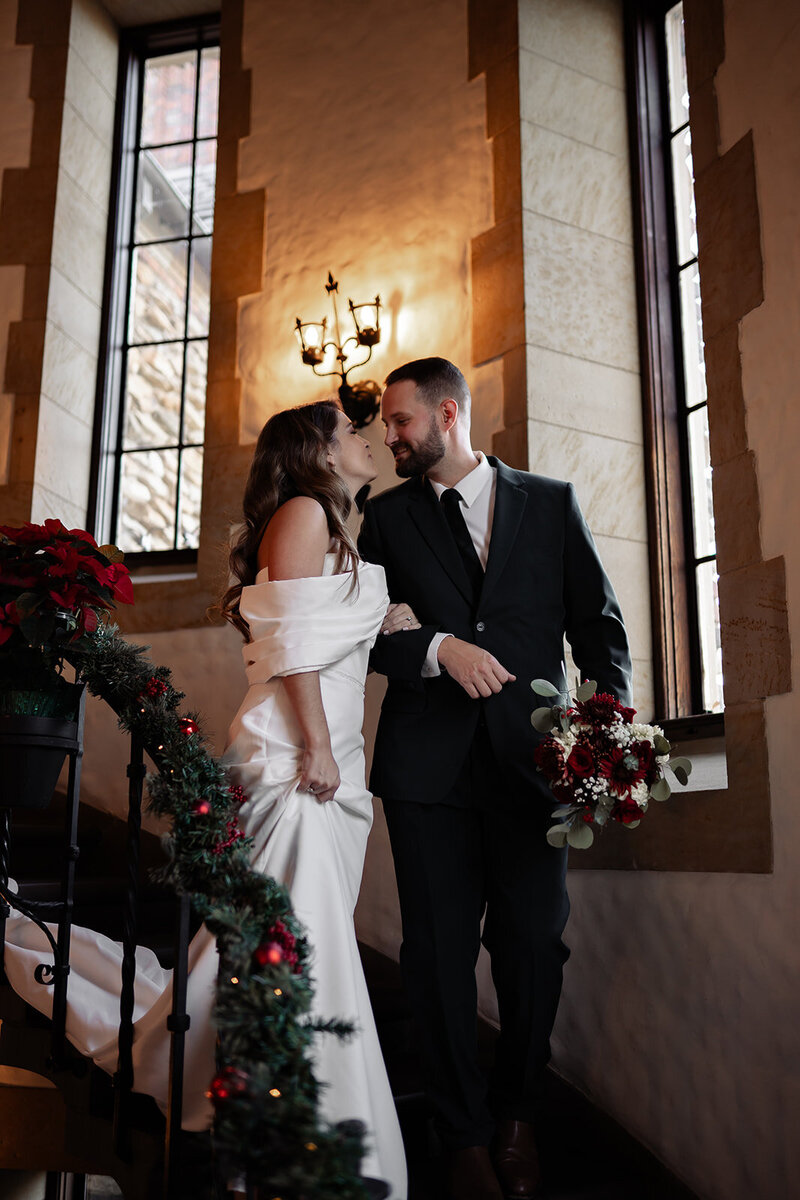 Bride and groom looking into each others eyes as they walk down Christmas decorated stairs indoors