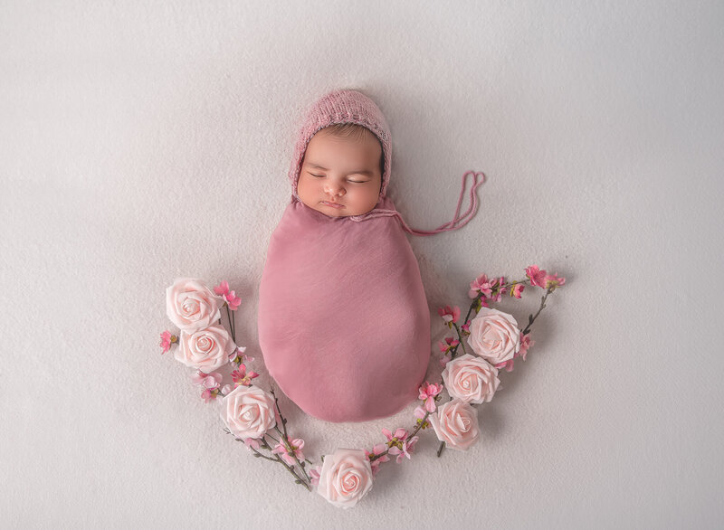 "Newborn baby peacefully sleeping, gently wrapped in soft fabric and surrounded by delicate flowers, captured in a serene and beautiful fine art photography session in Ottawa."